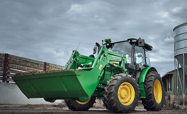Tractor with loader in front of fence and farm equipment