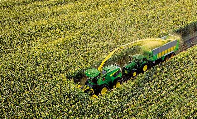 Harvester harvesting crops with a tractor following behind it.