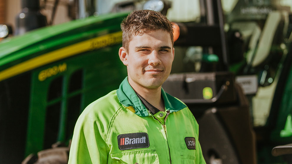 Josh Alexander standing in front of a John Deere tractor wearing a green Brandt work jacket