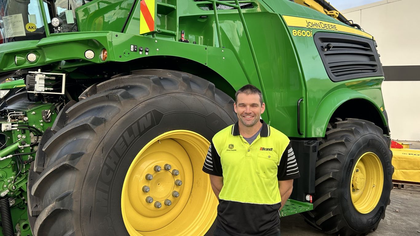 A man wearing a yellow high visibility shirt standing next to a large green agricultural machine.