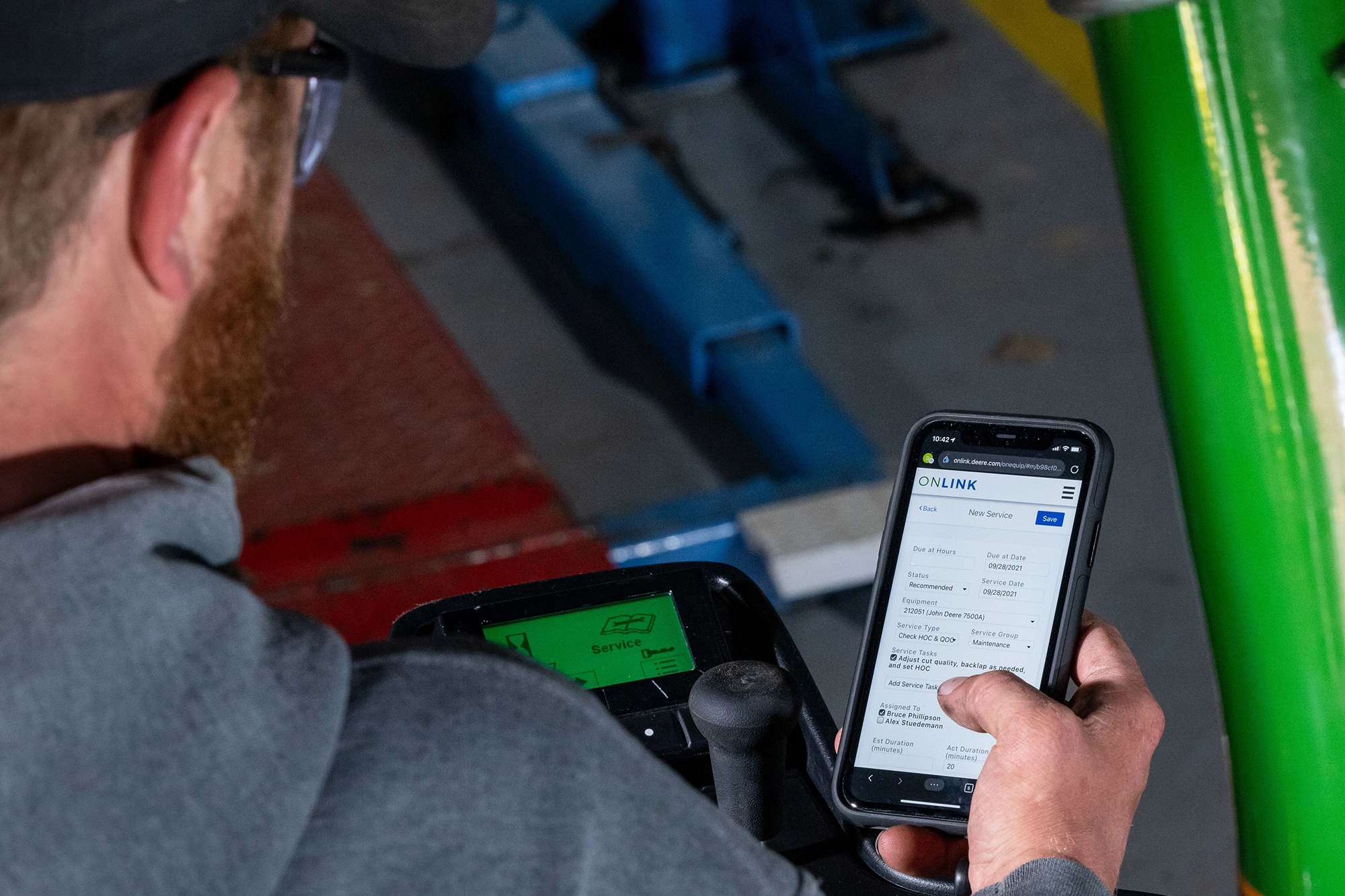 Man sitting on stationary fairway mower looking at his phone with the OnLink App.