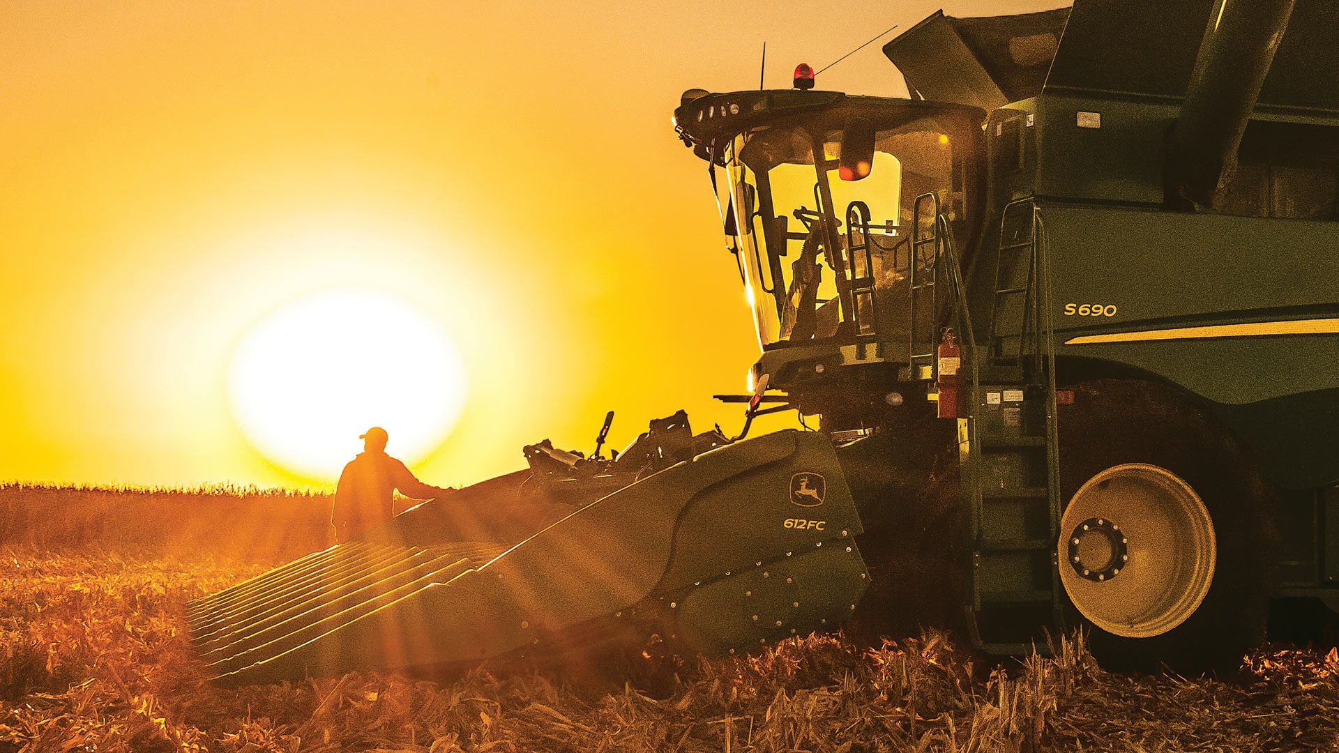 Corn header attached to a combine harvester at sunset.