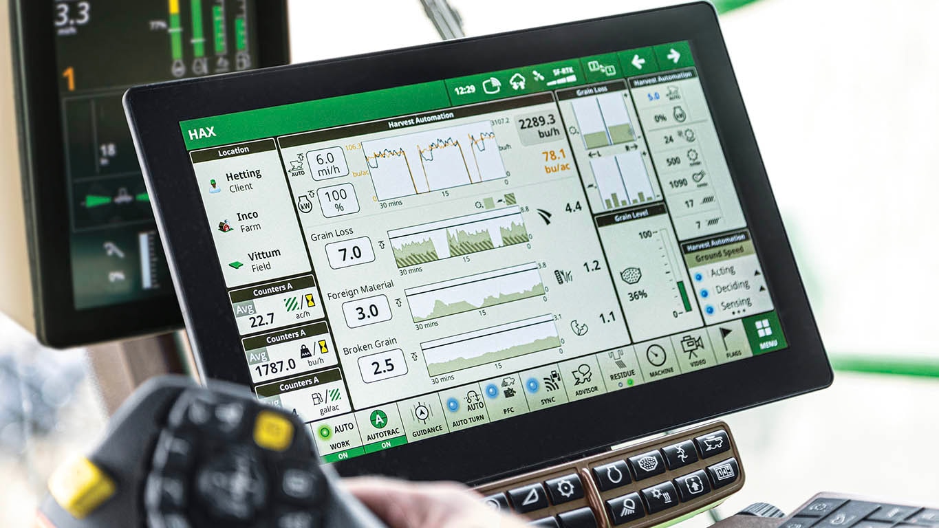 In-cab photo of a farmer in a John Deere Combine, adjusting his Harvest Settings Automation run page on a G5Plus CommandCenter™ Display