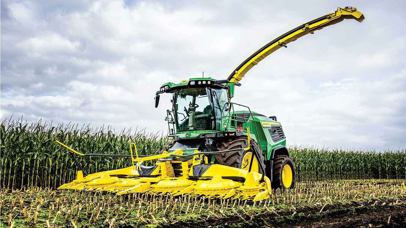 Green and yellow machine harvesting corn in a field under a cloudy sky.