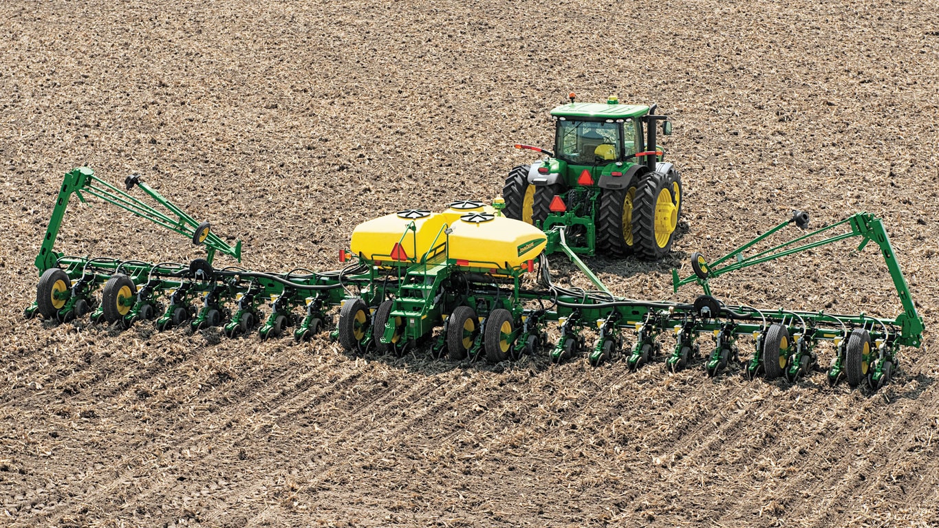 Green and yellow tractor pulls large planter with multiple rows across a plowed field.