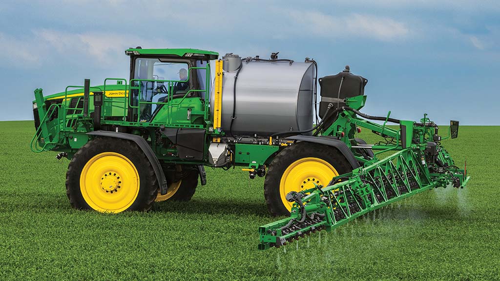 Side-view photo of a John Deere Self-Propelled Sprayer – with extended booms – applying in a field.