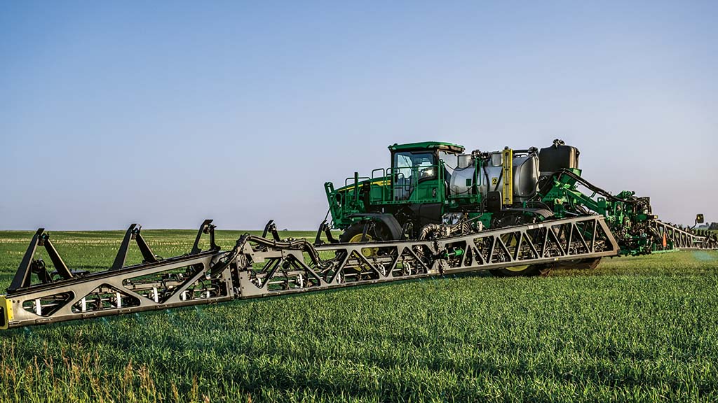 Side-view of a John Deere See & Spray Gen 2 Sprayer – with extended booms – applying in a field.