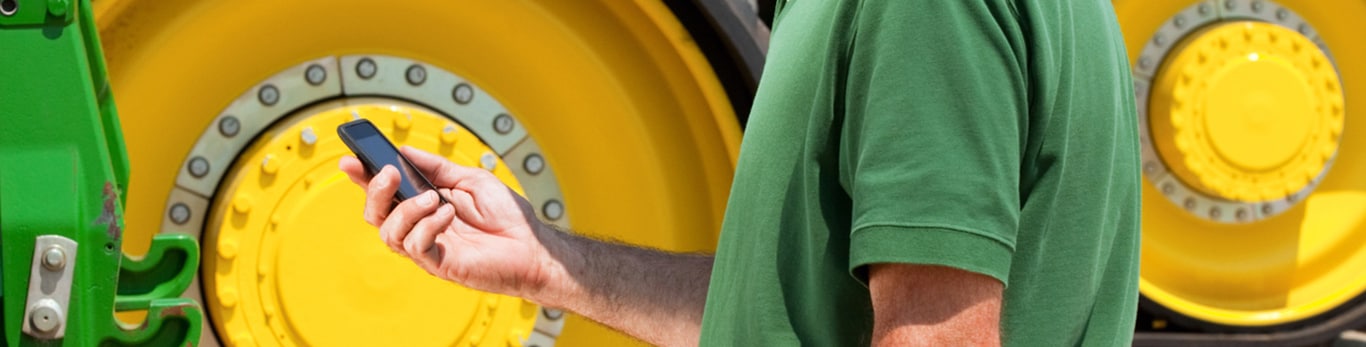 Man looking at a cell phone in front of a tractor