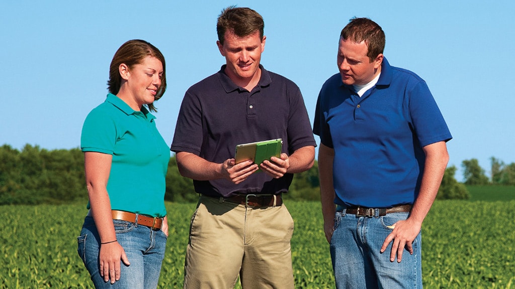 Three people looking at a tablet in a field