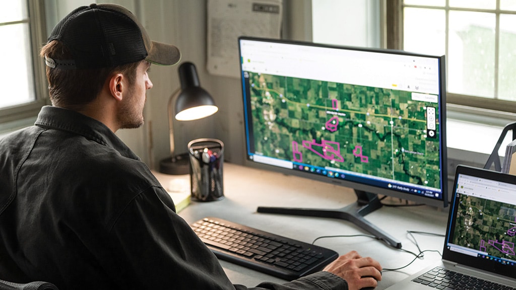 Man sitting at desk in front of a computer display, working in John Deere Operations Center.