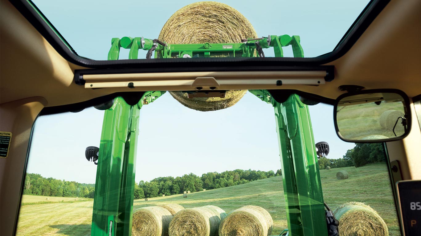 John Deere 6M Utility Tractor overlooking hay in the field