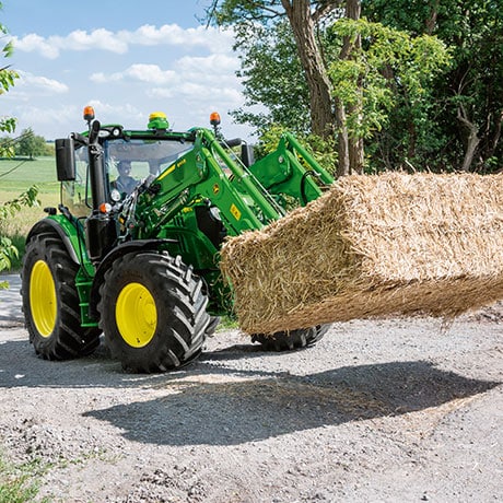 tractor lifting round hay bale with front loader